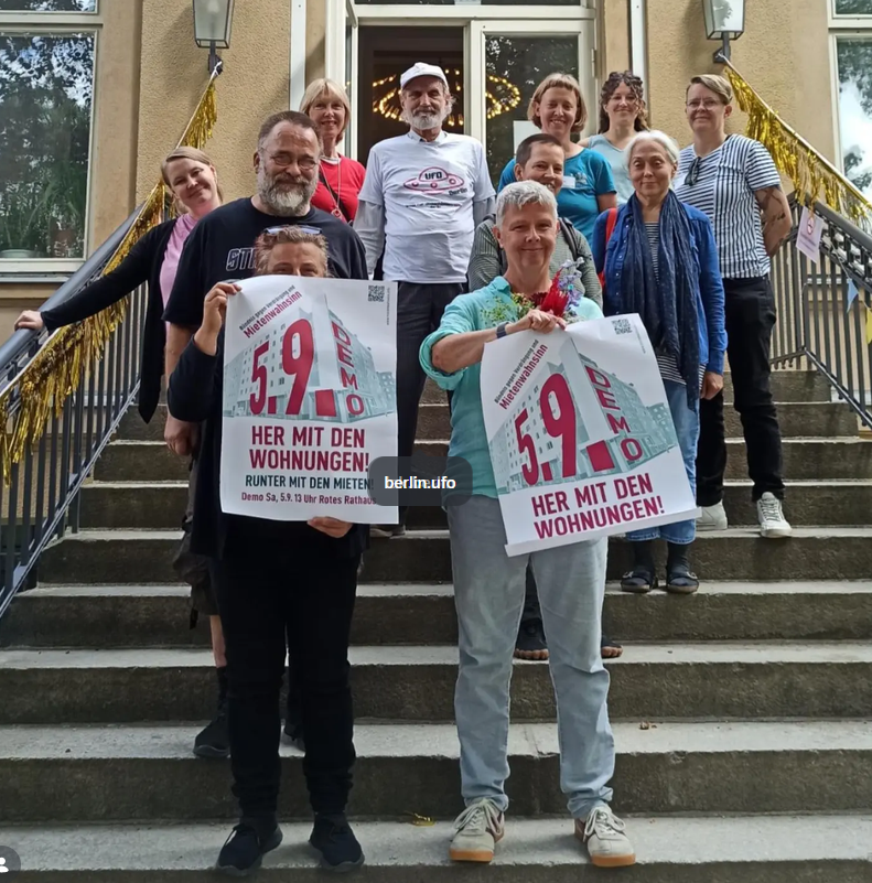 Gruppe von Menschen vor einem Nachbarschaftshaus in Berlin mit Plakaten zur Demonstration ‚Her mit den Wohnungen!‘ am 5. September 2026.